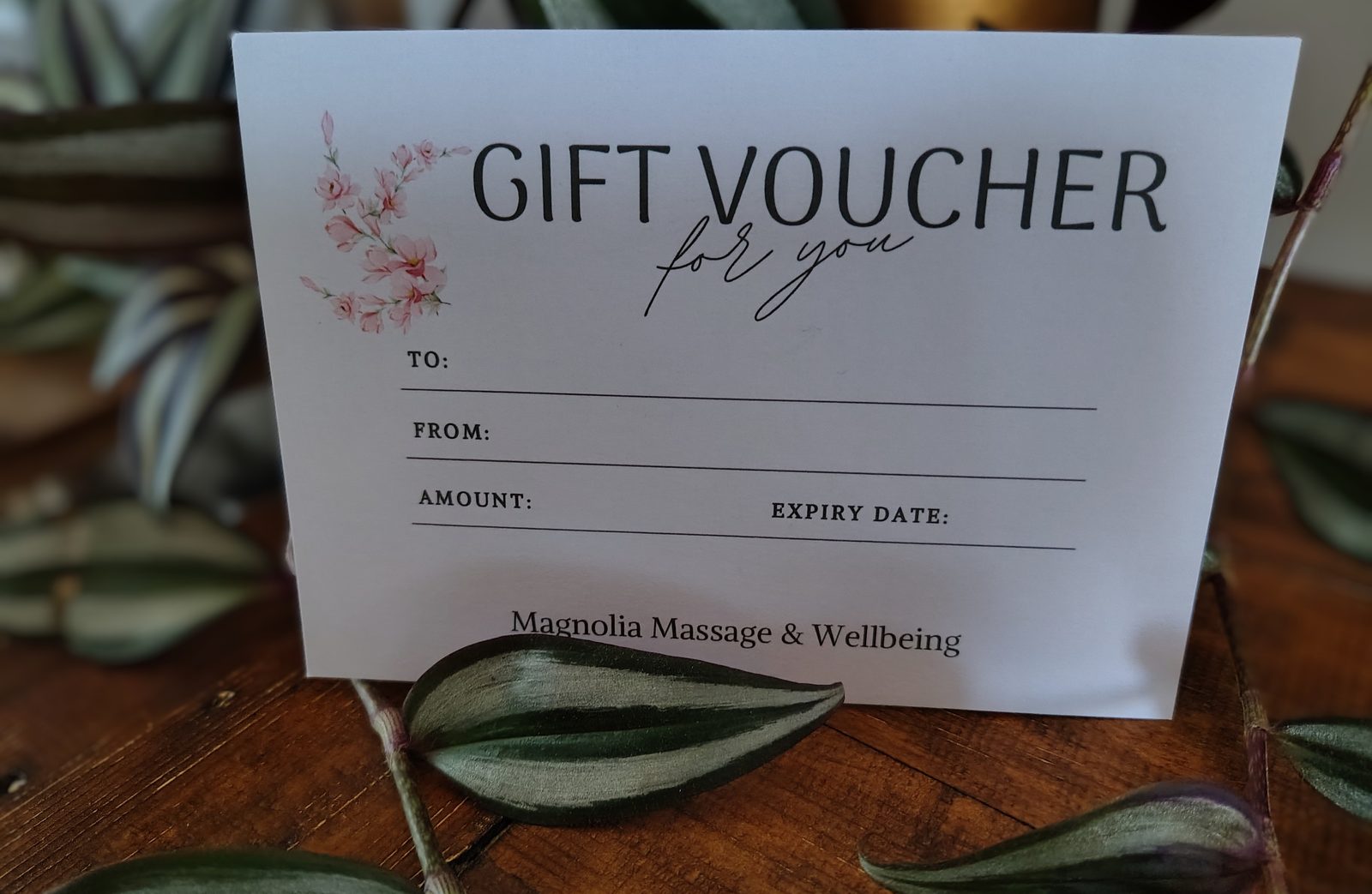 A Magnolia Massage & Wellbeing gift voucher card, printed with a magnolia sprig and spaces for a name, amount and expiry date.