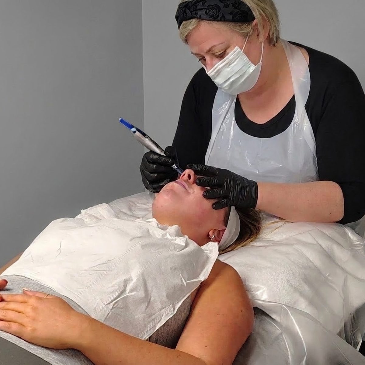 Louise carrying out a microneedling treatment on a client&rsquo;s face, wearing gloves, apron and mask.